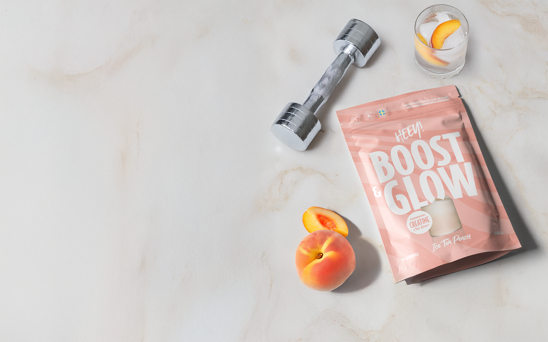Heey! Boost & Glow med Coll-egan® vegansk kollagenbyggare och kreatin, flatlay på marmor med hantel och persika