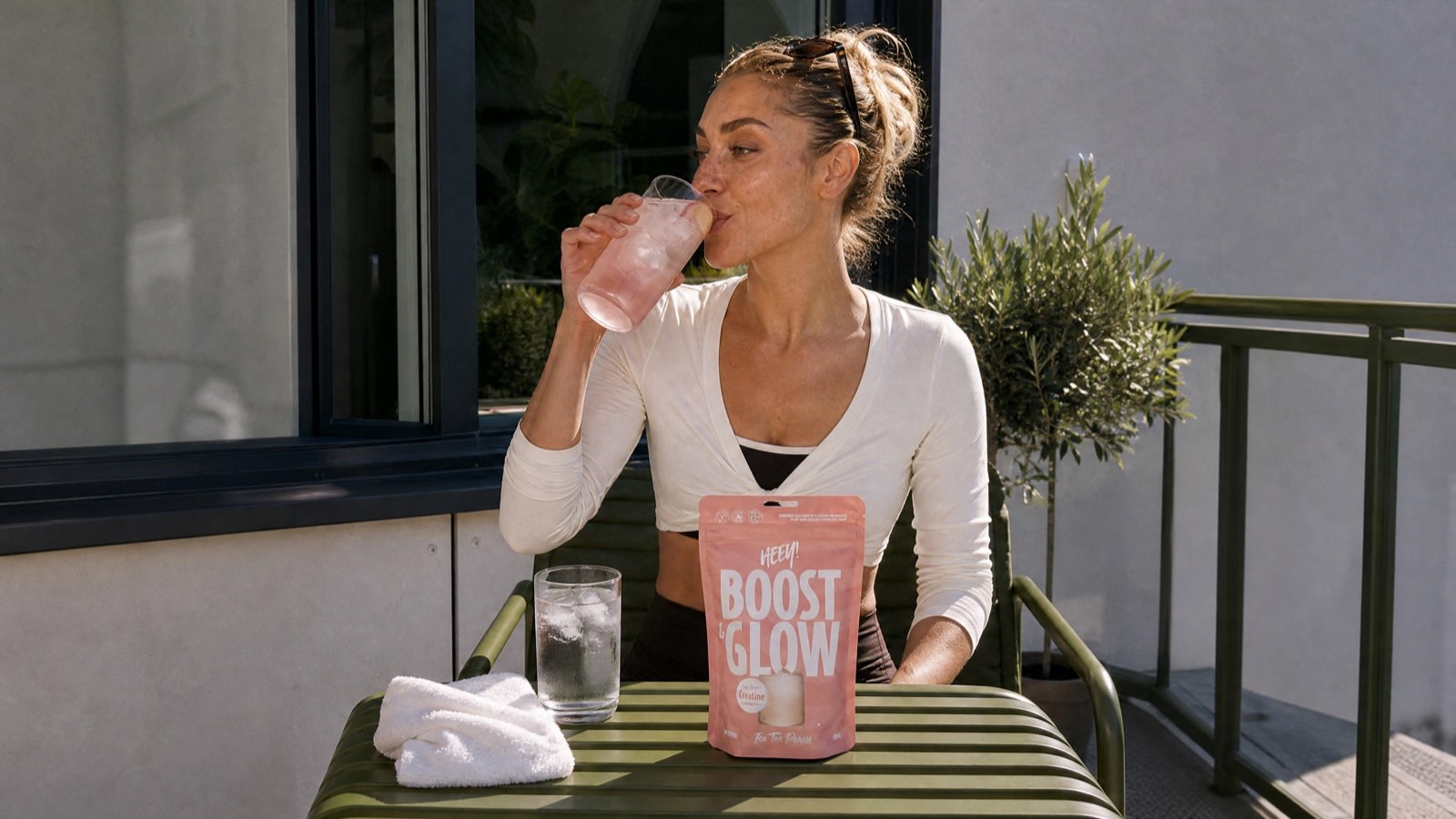 Kvinna dricker Boost & Glow Ice Tea Peach på balkongen efter löprundan, kreatin och vätska